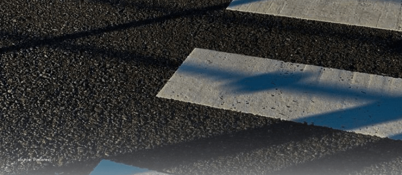 Crosswalk shadows on asphalt, echoing secondaries at a strategic crossroads.